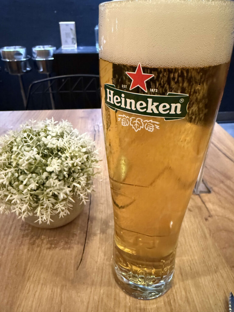 木製のテーブルの上に置かれた、泡の立った冷えたハイネケンのビールグラスと白い観葉植物