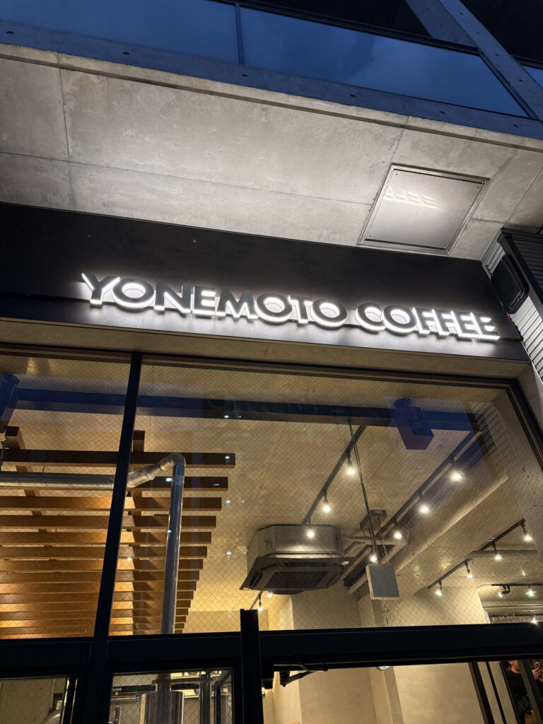 Glowing white YONEMOTO COFFEE sign on a glass-fronted building exterior at night