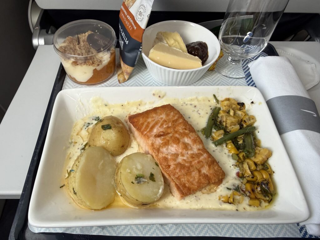 機内食のトレーに載せられたサーモンのソテーとクリームソース、付け合わせのジャガイモ、チーズプレート、デザート