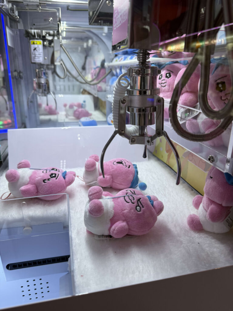 Metal claw aiming at pink Opanchu Usagi plush toys in a crawling pose inside a claw machine