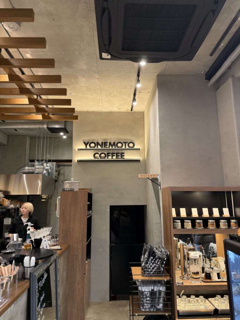 コンクリート打ちっぱなしの壁に掲げられたYONEMOTO COFFEEのロゴサインと、店内のカウンターの様子