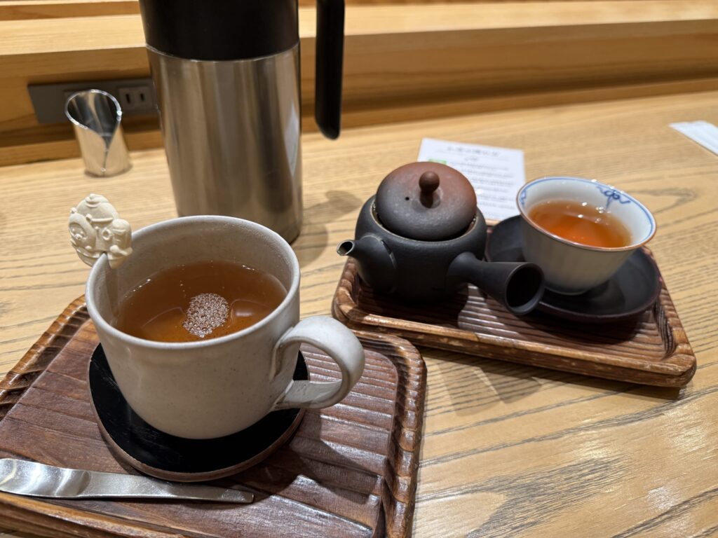 A tea set on a wooden table featuring a mug with a bear-shaped wafer on the rim, alongside a traditional teapot and cup.