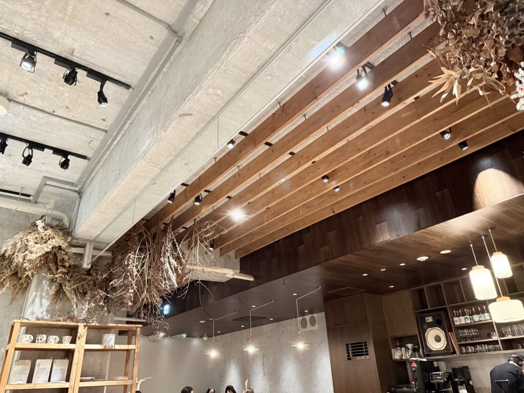 Interior of a renovated cafe featuring an exposed concrete ceiling decorated with wooden louvers and hanging dried flowers.
