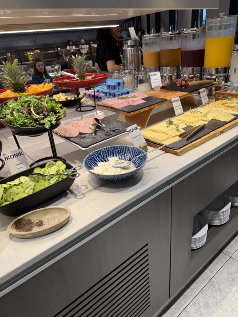 IKONIKホテルの朝食ビュッフェに並ぶサラダ、スライスハム、チーズ、ジュースサーバー