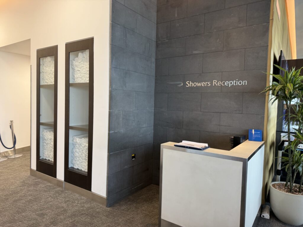 British Airways lounge shower reception desk featuring a grey tiled wall with 'Showers Reception' sign and shelves stocked with white towels