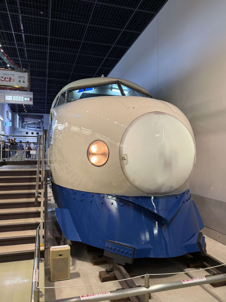博物館に展示されている初代新幹線0系の先頭車両。白と青のツートンカラーで、特徴的な丸い団子鼻のデザイン。