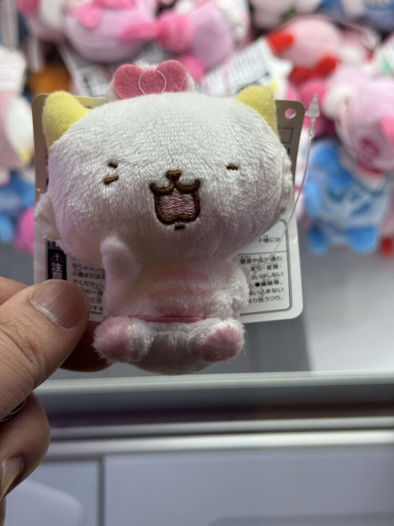 黄色い耳とウィンクした表情が愛らしい、白い猫のマスコットのぬいぐるみ