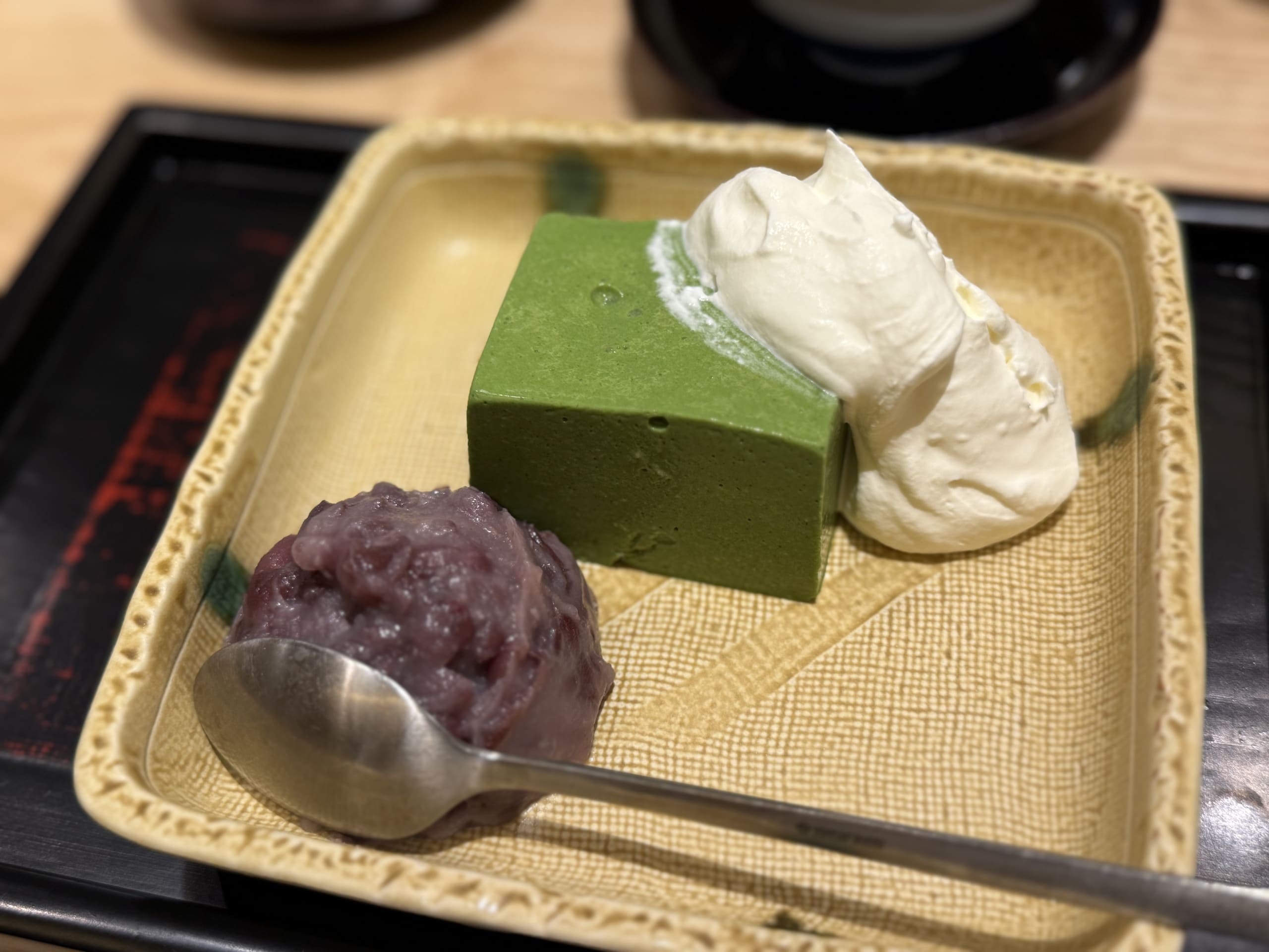 黄色い和皿に盛られた濃厚な緑色の抹茶ババロア。横にたっぷりの生クリームと粒あん、銀色のスプーンが添えられている。