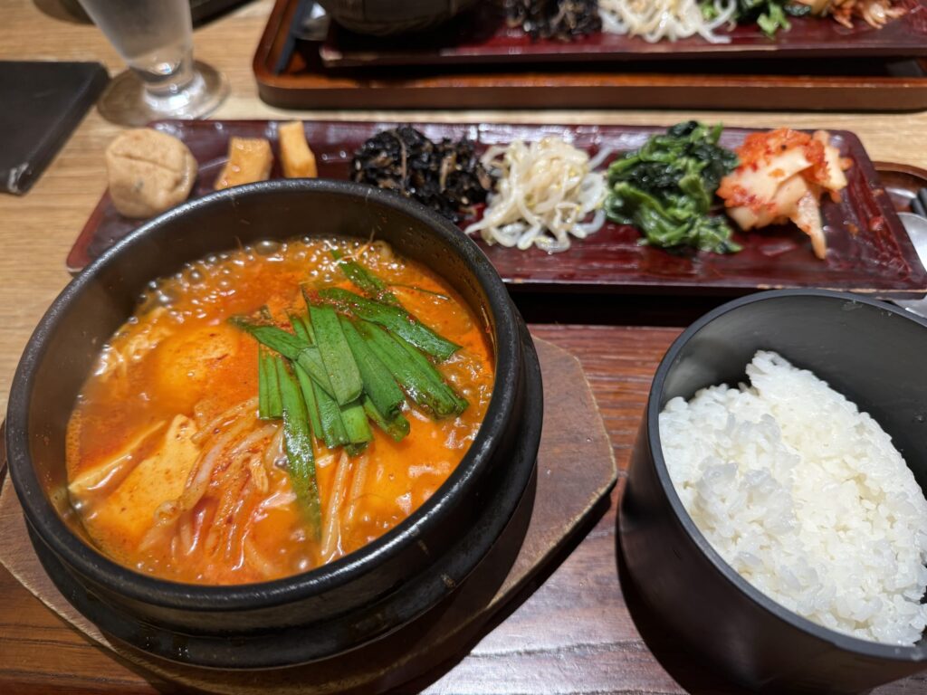 黒い土鍋に入った赤いスンドゥブチゲ、白米、ナムルとキムチの盛り合わせ定食