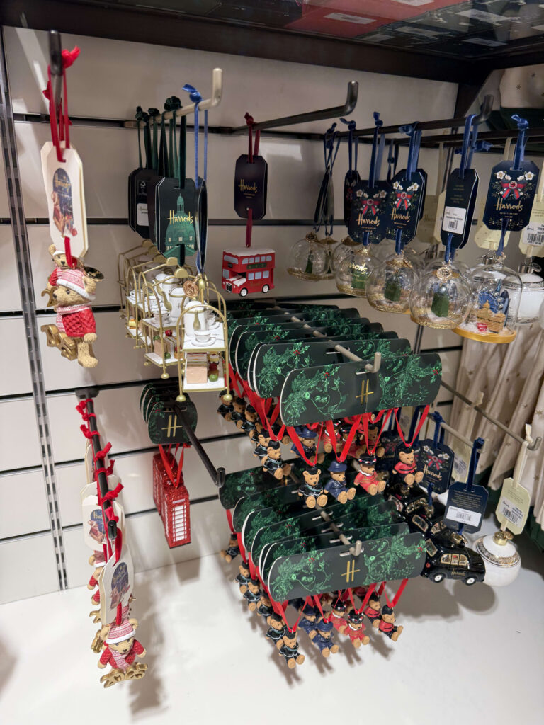 Harrods Christmas ornaments on display, featuring teddy bears in red sweaters, afternoon tea sets, and red double-decker buses