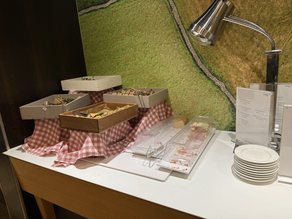 赤と白のチェック柄のクロスの上に木箱に入ったサンドイッチが並ぶビュッフェカウンターと照明用のランプ