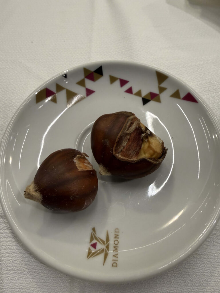 Two roasted chestnuts served on a small white saucer with a gold DIAMOND logo and geometric patterns