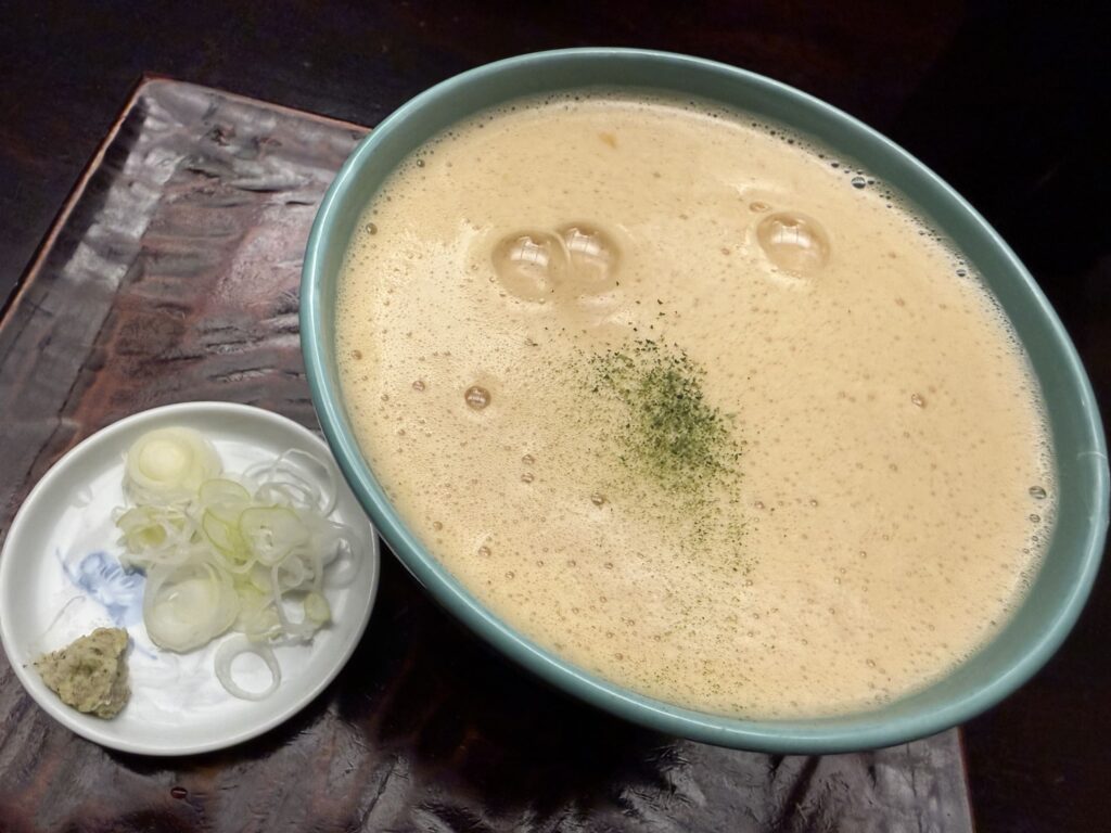 A bowl of Tororo Soba covered in foamy grated yam broth, served with scallions and wasabi on the side