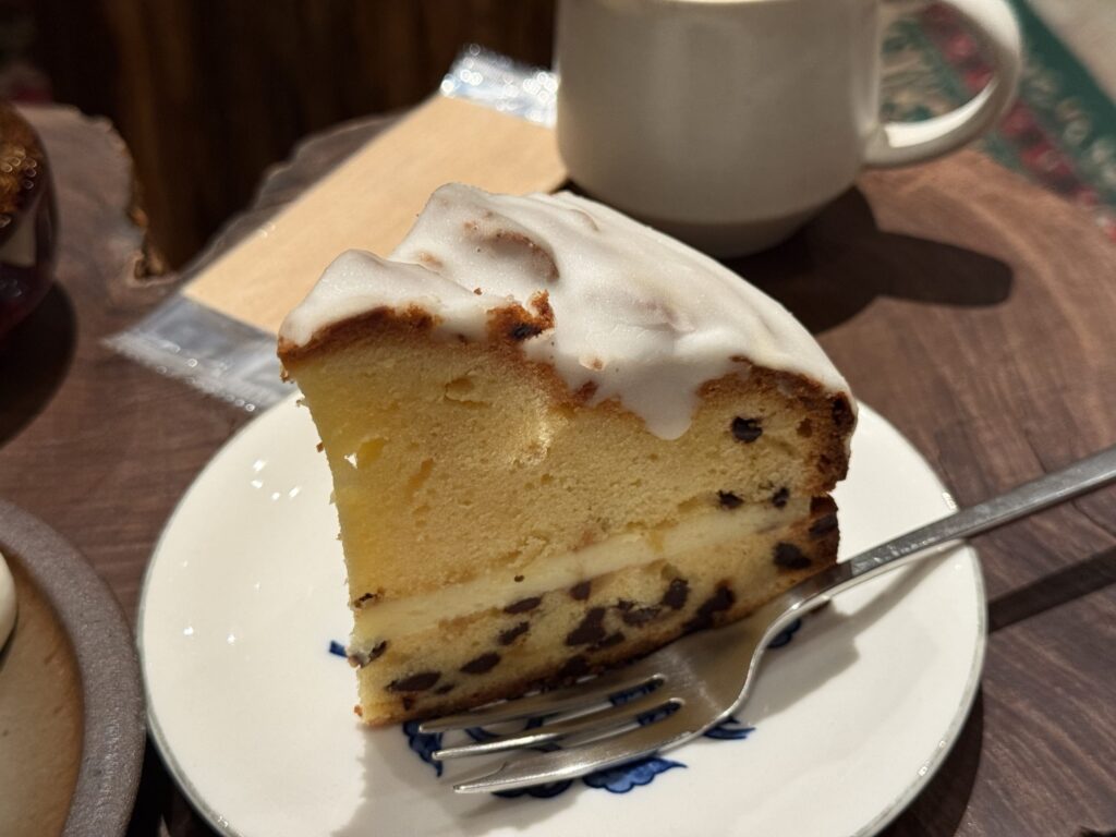 Slice of glazed pound cake with a cream layer and chocolate chips, served with a cup of coffee