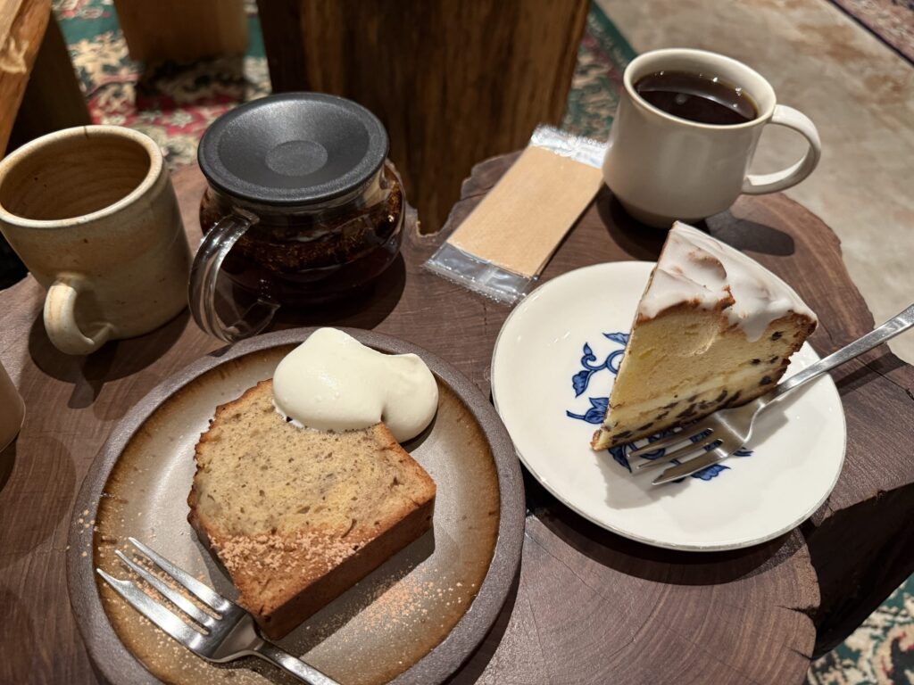 Overhead view of coffee, a glass teapot, banana cake with whipped cream, and an iced pound cake arranged on a stump-like wooden table