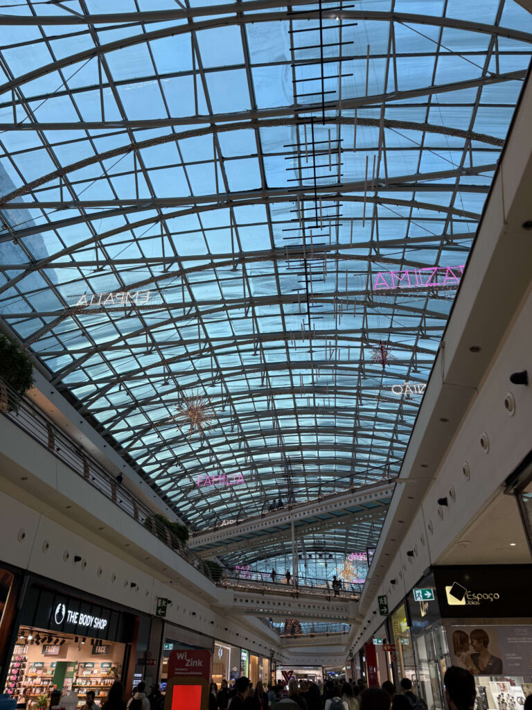 Low-angle view of the large glass ceiling at Vasco da Gama Shopping Mall decorated with Christmas lights and neon signs.
