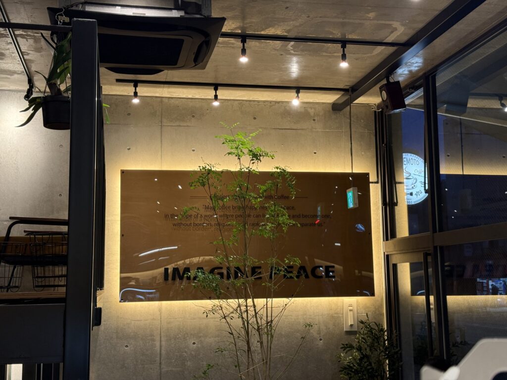 コンクリートの壁に設置された「IMAGINE PEACE」のバックライト看板と、手前の背の高い観葉植物