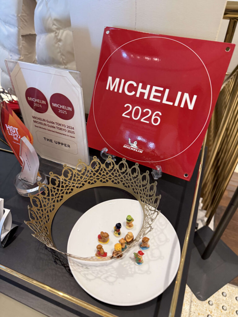 Red Michelin 2026 plate, 2024 and 2025 certificates, THE UPPER logo, and a decorated plate in the foreground