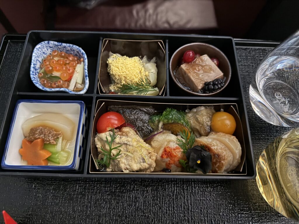 A luxurious Japanese in-flight meal appetizer called 'Irodori Gozen' served in a black bento box with salmon roe, simmered vegetables, and seafood.