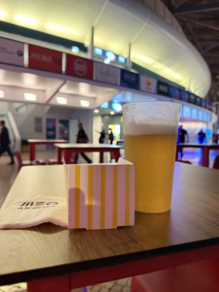 MEOアリーナのコンコースにあるテーブル上のビールと黄色と白のストライプ柄のスナックボックス、ロゴ入りナプキン