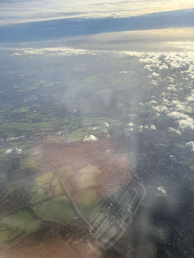 飛行機の窓から見下ろす、ロンドン・ヒースロー空港へ降下中のイギリスの緑豊かな田園風景と雲
