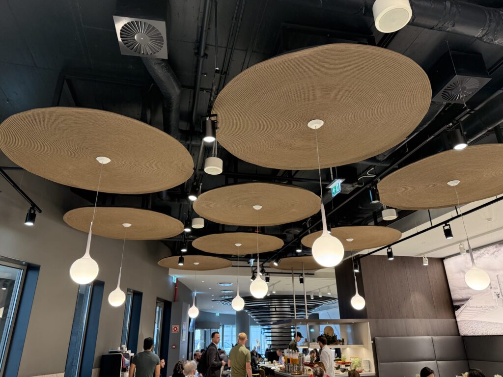 Ceiling of a modern breakfast venue featuring large circular woven discs and white teardrop pendant lights