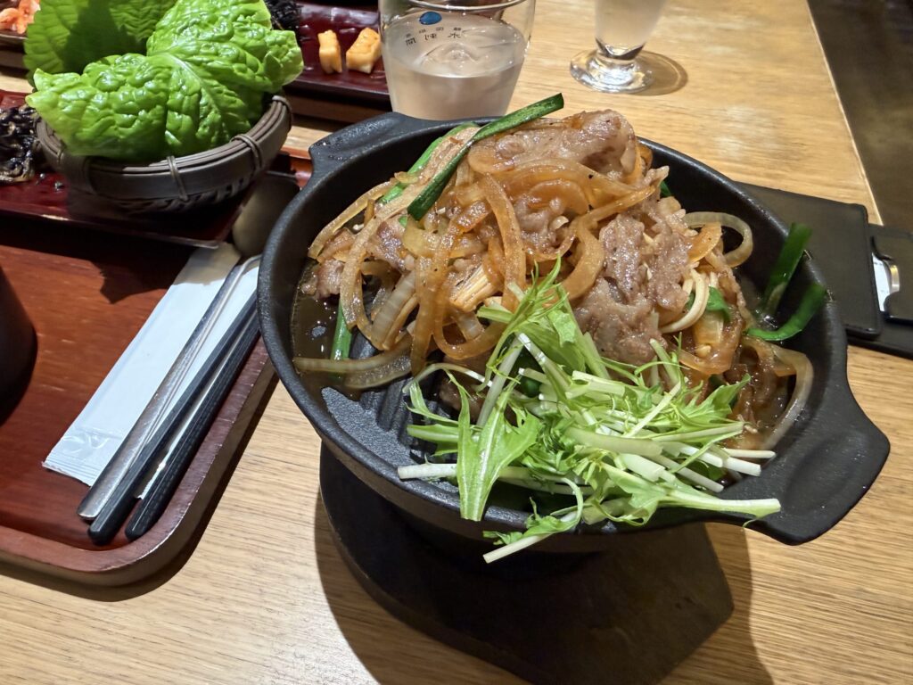 Bulgogi beef and onions served on a black iron skillet topped with mizuna greens