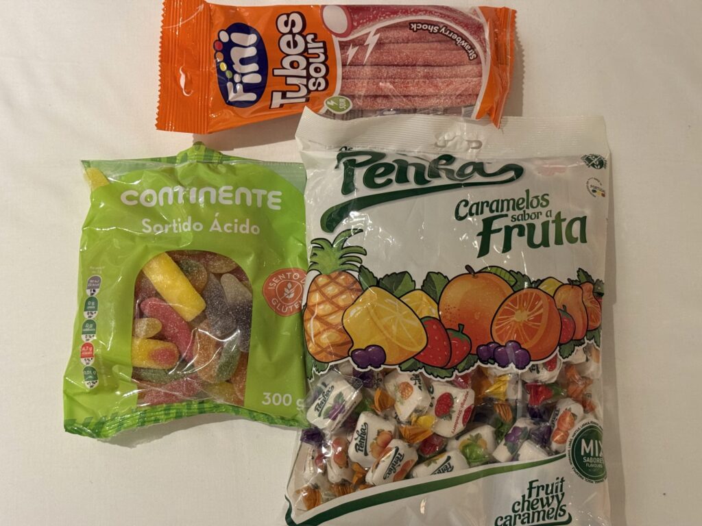 白い背景に置かれた3つのキャンディのパッケージ：上のオレンジ色の袋はFiniのサワーチューブ、左下の緑色の袋はContinenteのサワーグミ、右下の白い袋はPenhaのフルーツキャラメル。