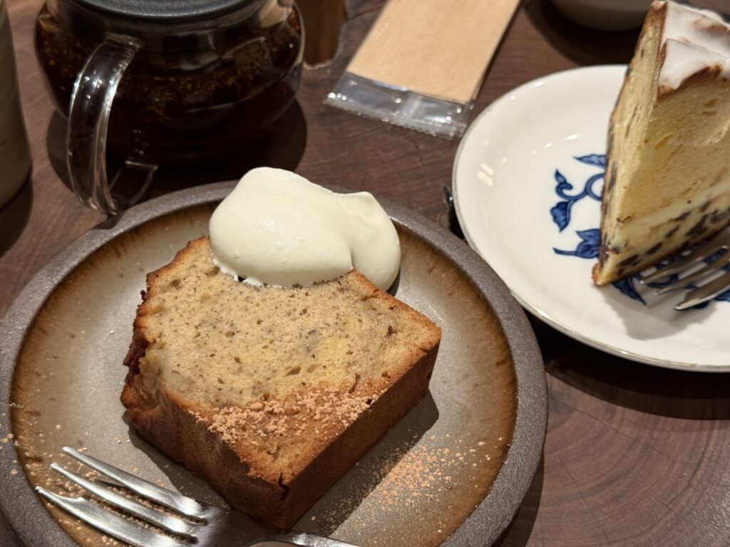 A thick slice of banana cake topped with fresh cream and a dusting of cinnamon on a rustic plate.