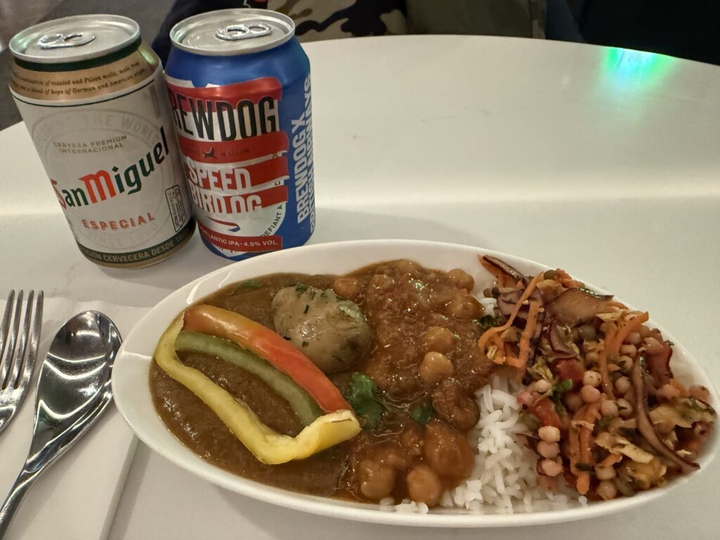 A plate of curry, rice, and salad served with cans of San Miguel and BrewDog beer