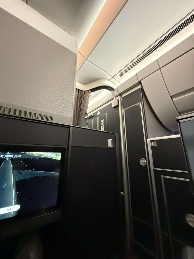 高いパーティションの壁と尾翼カメラの映像が映る飛行機の機内座席