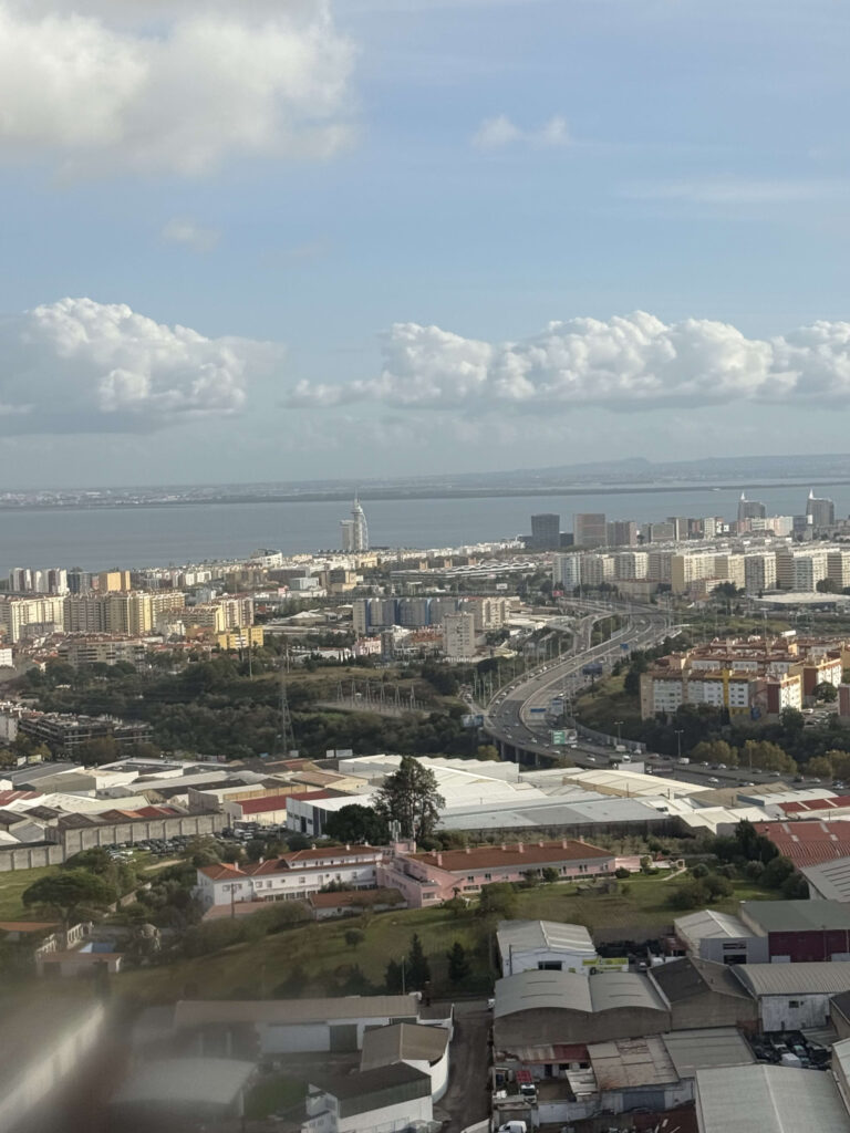 Aerial view of the Lisbon cityscape featuring the Tagus River and Vasco da Gama Tower under a blue sky with clouds