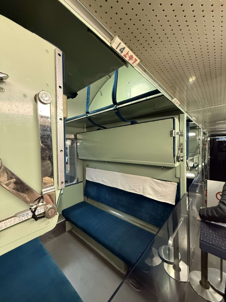 Interior of a JNR 20 series passenger car showing blue velvet seats and the structure of 3-tier Type B sleeper berths.