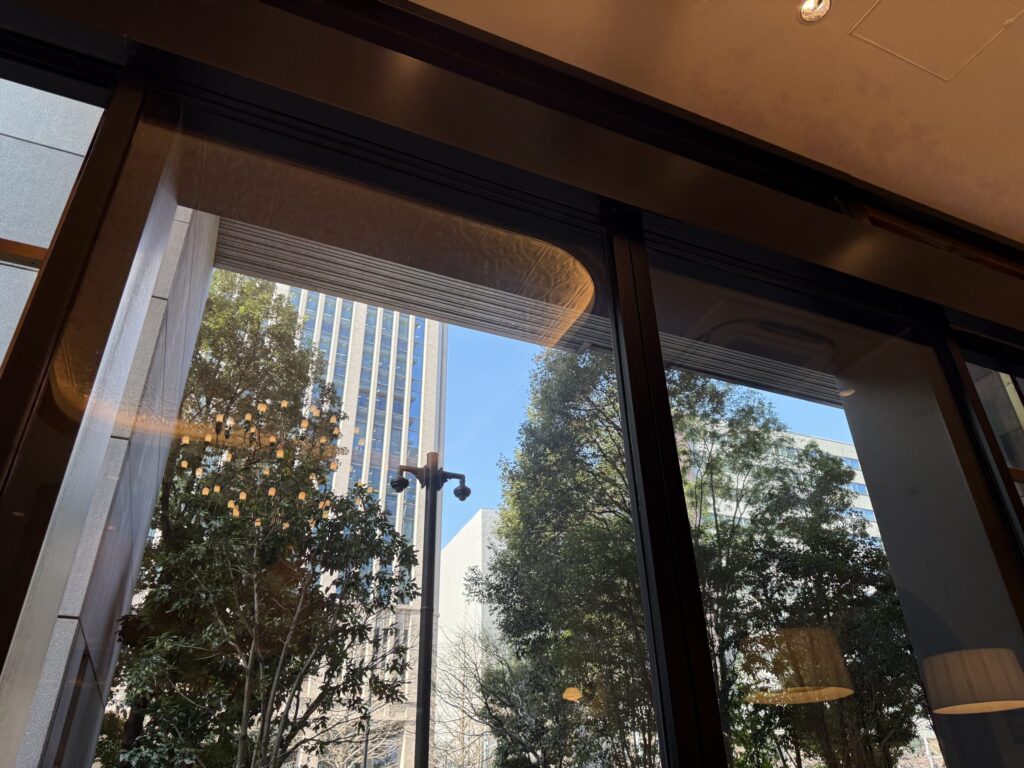 View of Toranomon buildings, blue sky, and lush street trees seen through a large window