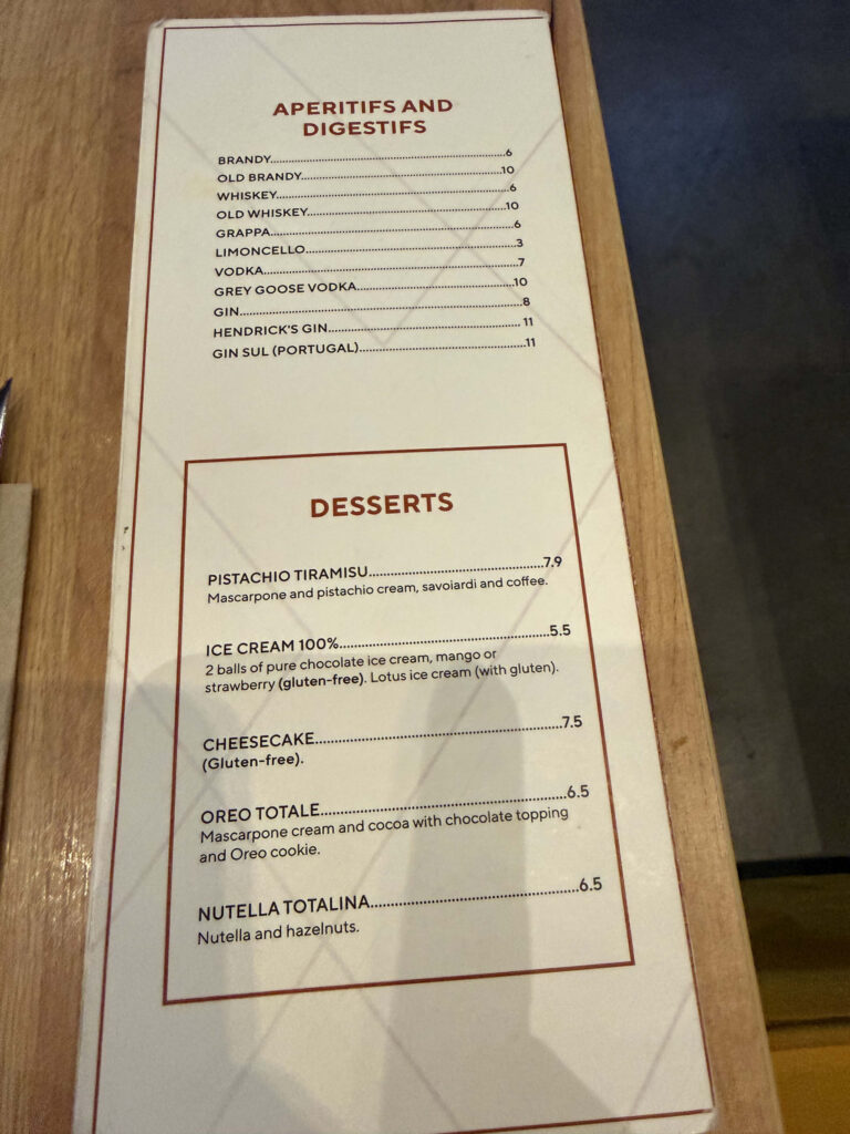 Restaurant menu card on a wooden table listing aperitifs, digestifs, and a selection of desserts