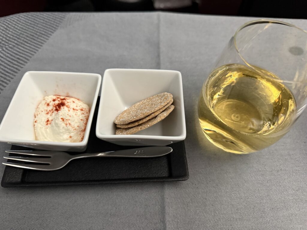 JAL inflight amuse-bouche featuring a creamy dip, crackers, and a glass of Delamotte champagne