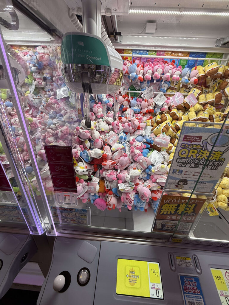 山のように積まれたスポンジ・ボブやパステルカラーのぬいぐるみが詰まった3本爪のUFOキャッチャー