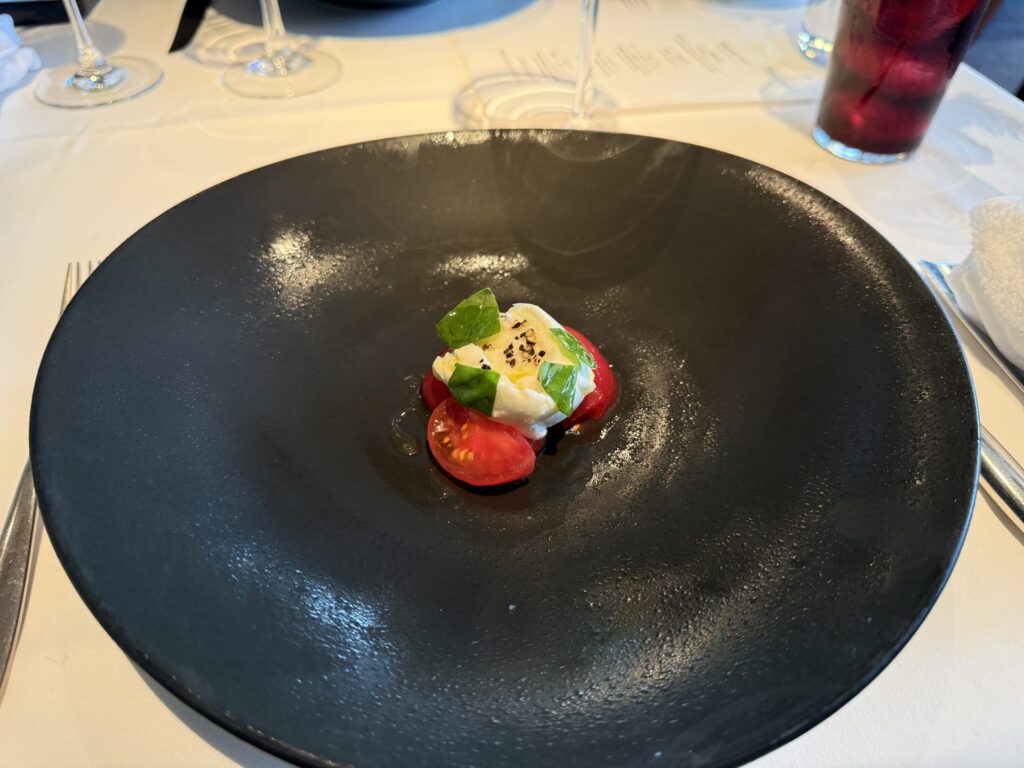 Caprese salad with buffalo mozzarella, tomatoes, and basil served in the center of a large black plate