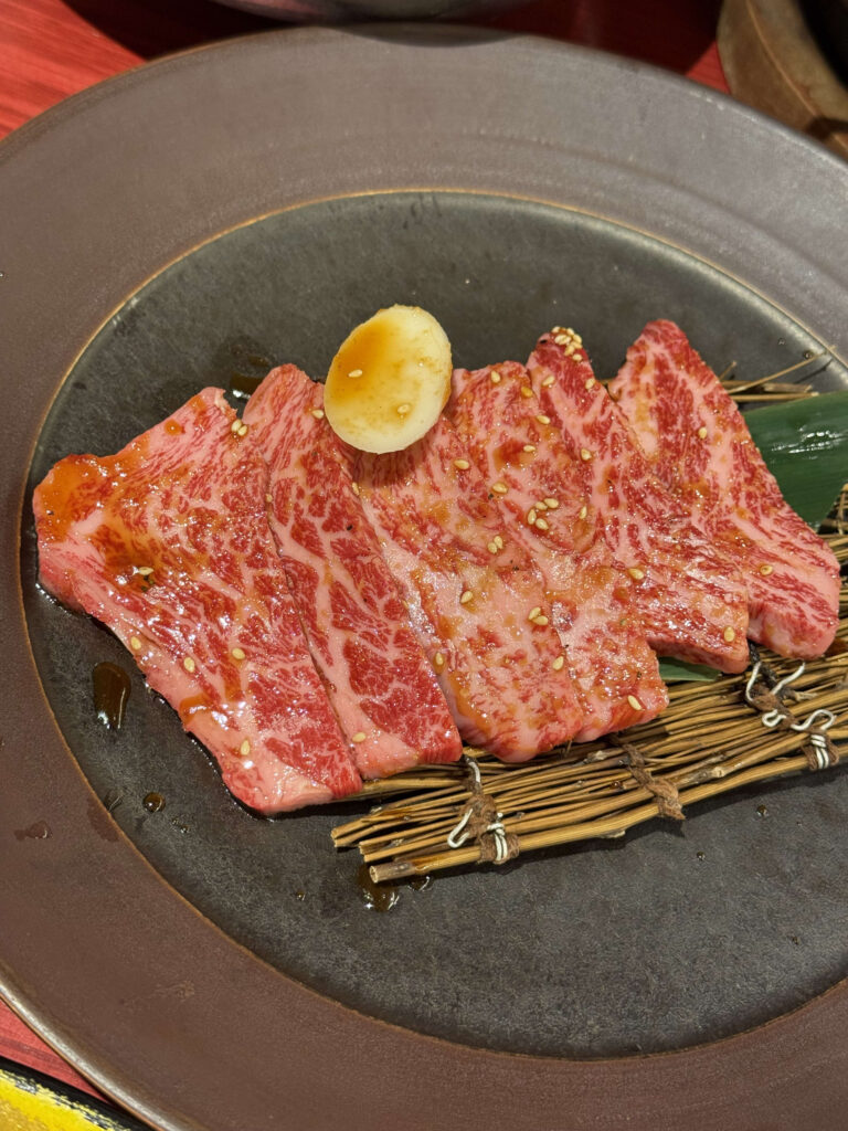 竹簾の上に盛られた、タレと胡麻が絡んだ霜降りカルビ焼肉とニンニク