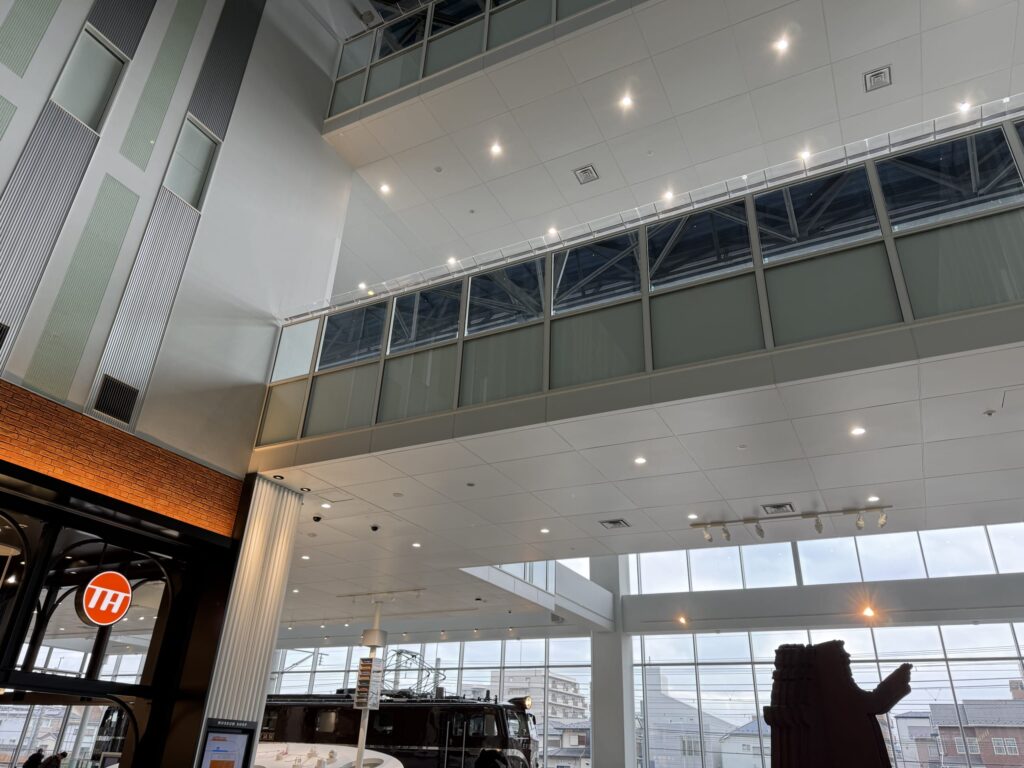 Low-angle view of the Railway Museum entrance hall atrium, featuring high ceilings, glass walkways, and a brick shop entrance with a TH logo
