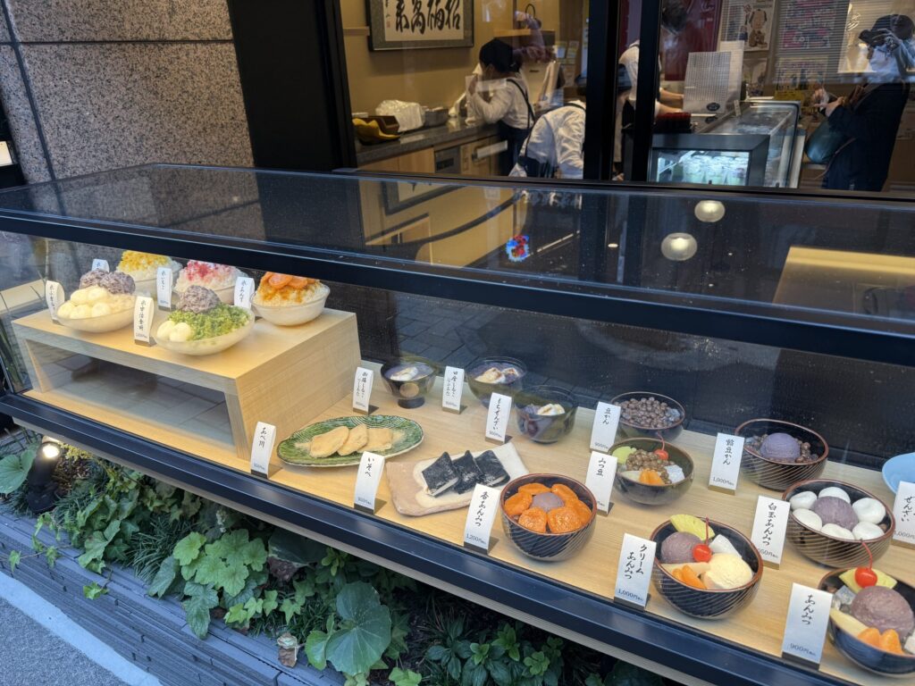 老舗甘味処の店頭ショーケースに並ぶ、かき氷やあんみつなどの色鮮やかな食品サンプル