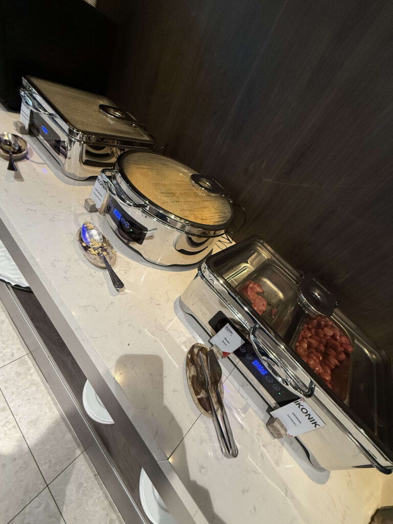 Stainless steel buffet warmers containing scrambled eggs, bacon, and sausages on a marble counter