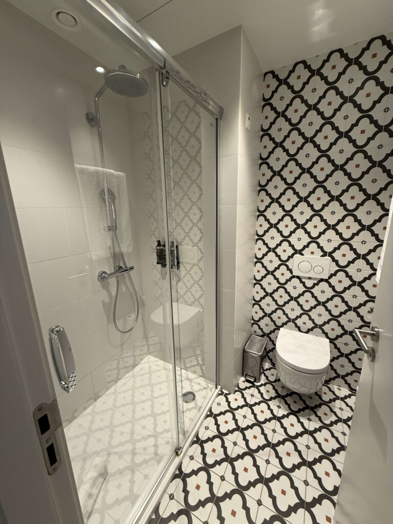 Modern bathroom interior featuring geometric patterned tiles, a glass-enclosed shower, and a wall-mounted toilet