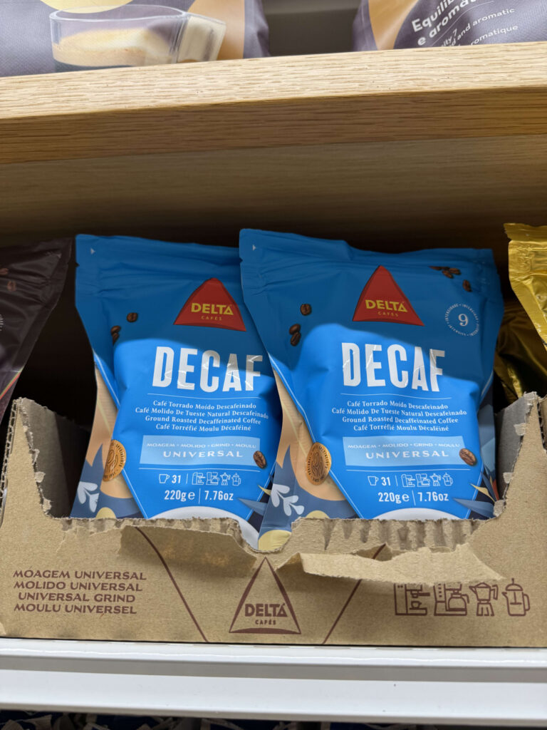 Two blue bags of Delta Cafés Decaf ground coffee on a wooden shelf