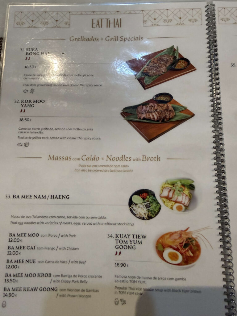 「EAT THAI」レストランのメニューページ。上段にはタイ風グリルビーフ（SUEA RONG HAI）やグリルポーク（KOR MOO YANG）などのグリル特選料理、下段にはトムヤムクンヌードルやバーミー（卵麺）などの麺料理が写真と価格付きで掲載されている。