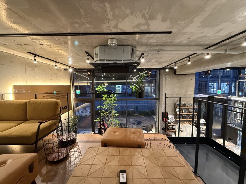 コンクリート打ちっぱなしのカフェ店内、中2階にある幾何学模様の木製テーブルとマスタード色のソファ席