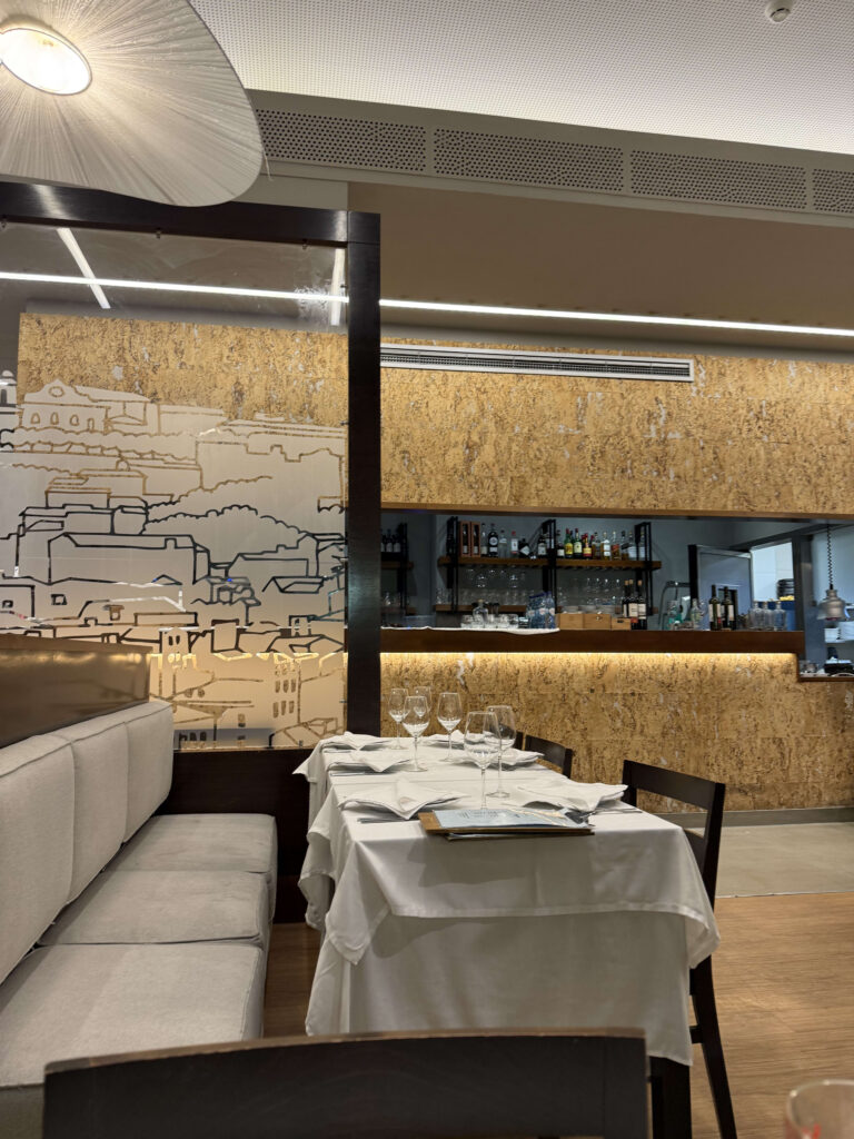 白いテーブルクロスがセットされたテーブルと、街並みの線画が描かれたガラスの間仕切りがあるレストランの内装