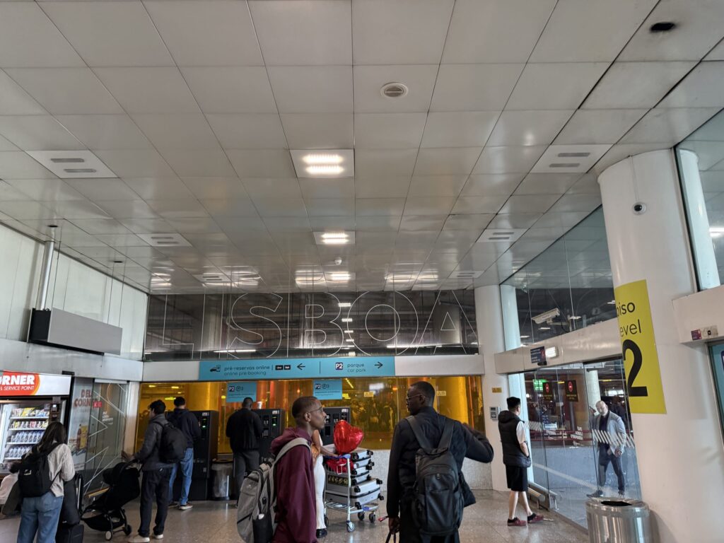 Interior of Lisbon Airport terminal with travelers, LISBOA signage, and signs showing the Uber logo