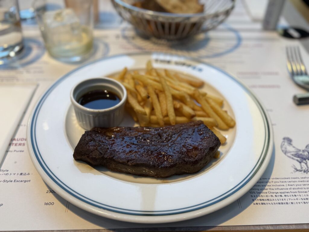 Steak frites with a pile of french fries and a small cup of dipping sauce on a white plate