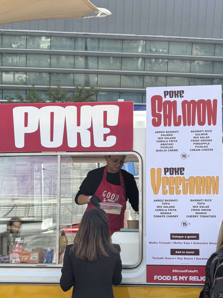 A staff member preparing food inside a red and white POKE food truck with a menu board showing Salmon and Vegetarian options.